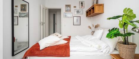 Une chambre avec un lit, une serviette rouge, une plante en pot et des œuvres d’art mural.