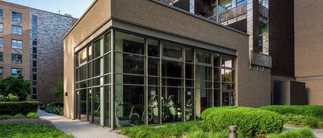 Un bâtiment moderne doté de grandes fenêtres en verre, d’une façade en briques et d’un jardin bien entretenu.