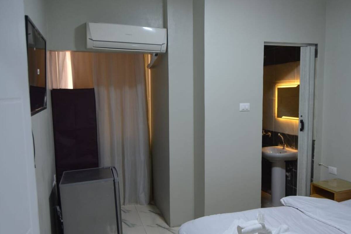 Habitación de hotel con una cama, una mesita de noche, un lavabo y un equipo de aire acondicionado.