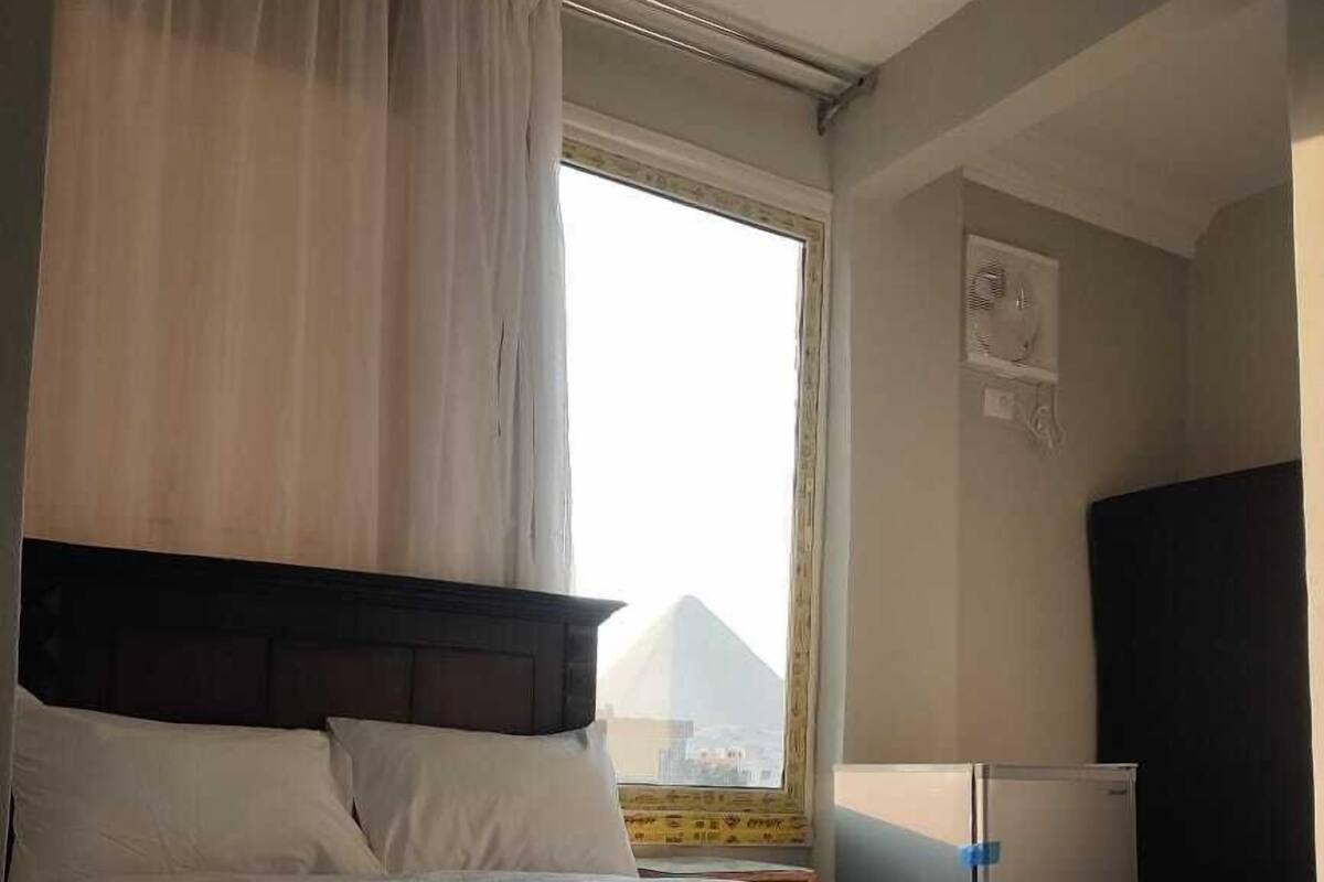 Una habitación de hotel con una cama grande, una ventana con cortinas, un escritorio pequeño con una lámpara y un televisor en la pared.
