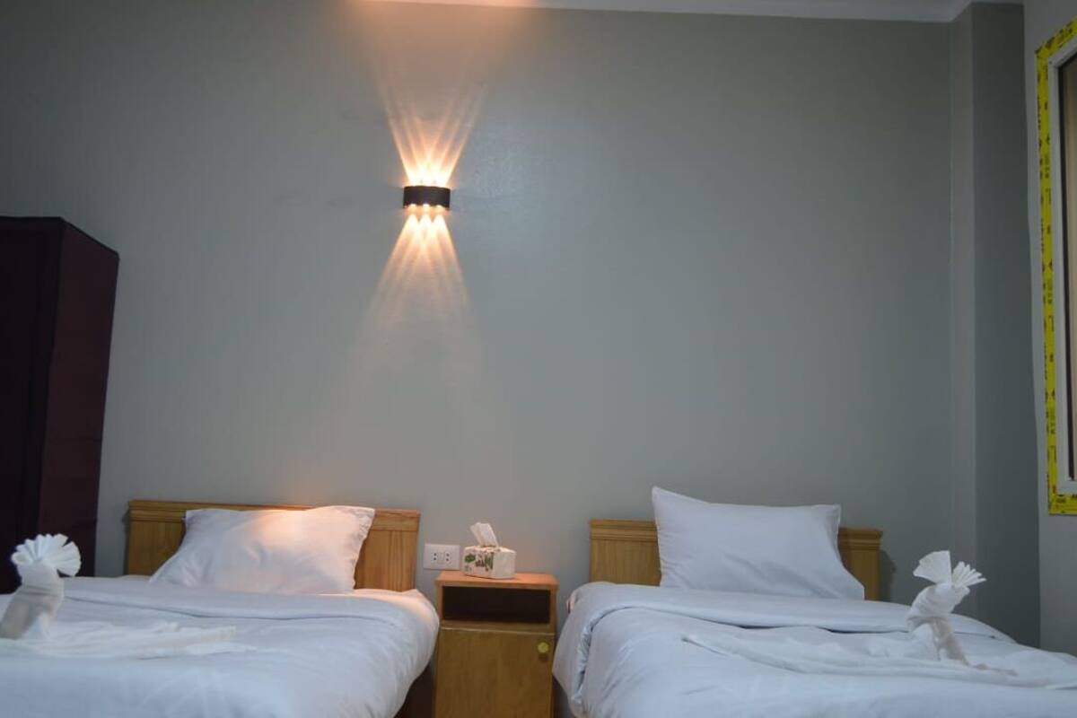 Una habitación de hotel con dos camas, una mesita de noche con lámpara y una lámpara de pared.