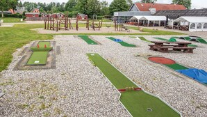 Zona recreativa al aire libre con un putting green, búnkeres de arena y mesas de picnic.