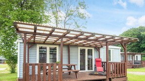 Una terraza de madera con un pérgola, una mesa de picnic y una silla roja.
