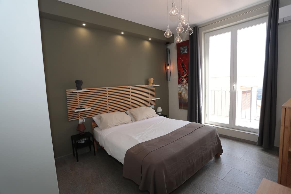 Une chambre moderne avec un grand lit, une table de chevet, une commode et une fenêtre avec des rideaux.