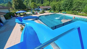 Una piscina con varias toboganes, rodeada por un patio con mobiliario exterior y vistas a la vegetación circundante.