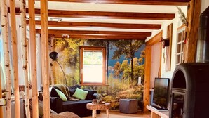 Una sala de estar acogedora con chimenea, un sofá, un televisor y un mural de un paisaje forestal.