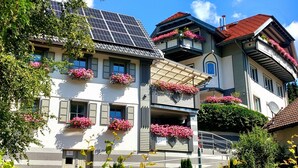 Un edificio de varios pisos con balcones decorados con flores rosadas, paneles solares y una antena parabólica.