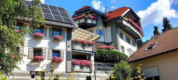 A multi-story building with balconies adorned with pink flowers, solar panels, and a satellite dish.