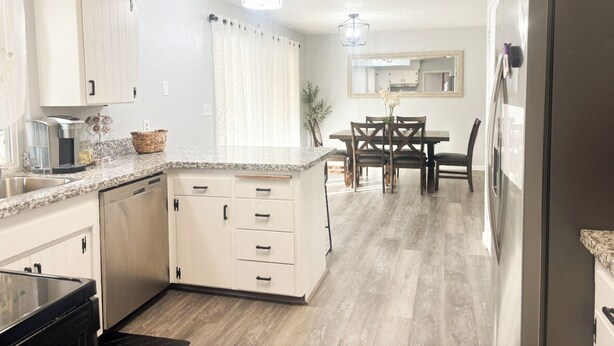 Una cocina moderna con armarios blancos, encimera de granito y comedor con mesa y sillas de madera.