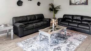 Una sala de estar con dos sofás de cuero negro, una mesa de centro de vidrio y un tapete estampado.