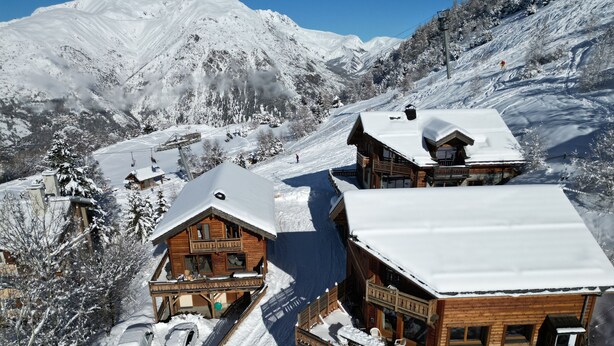 A snow-covered mountain resort with wooden buildings, ski lifts, and a parking area.