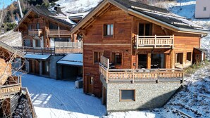 A wooden chalet with a balcony, a stone foundation, and a ski lift in the background.