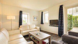 A modern living room with a sofa, a coffee table, a TV, and large windows with curtains. - Summio Duynparc De Heeren van 's-gravensande ('s-Gravenzande)