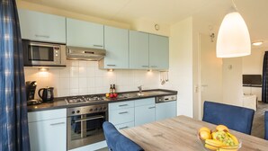 A modern kitchen with a gas stove, oven, microwave, and light blue cabinets. There is a dining table with chairs and a fruit bowl. - Summio Duynparc De Heeren van 's-gravensande ('s-Gravenzande)