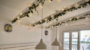 Un coin repas avec une table blanche dressée pour quatre personnes, deux lampes suspendues et une vue sur l’extérieur grâce à une porte vitrée.