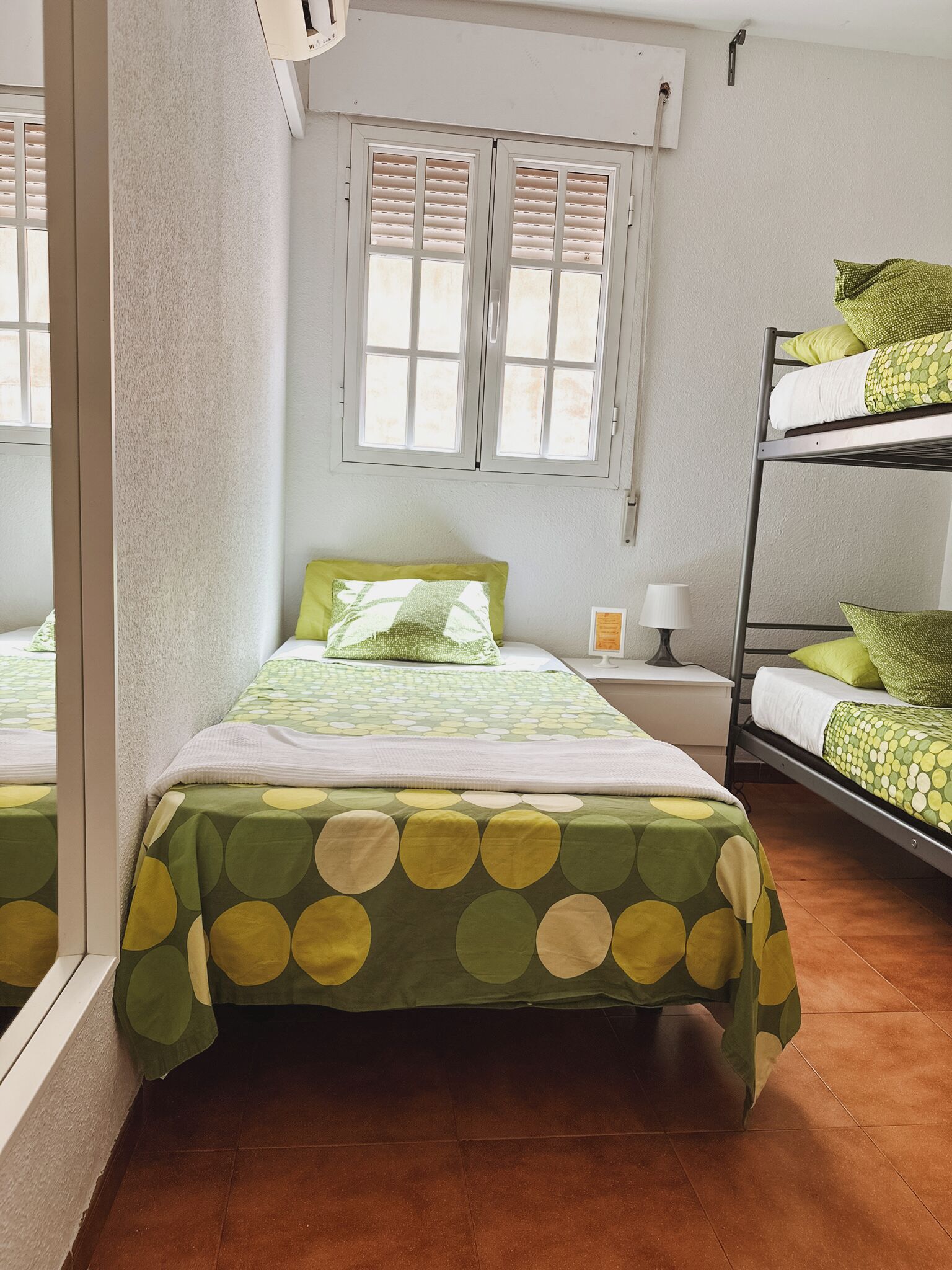 Een kamer met twee bedden, een raam met luiken, een bedlampje en een stapelbed.