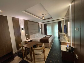 Una habitación de hotel moderna con una cama grande, un escritorio, una silla, un televisor y un baño con espejo y lavamanos.