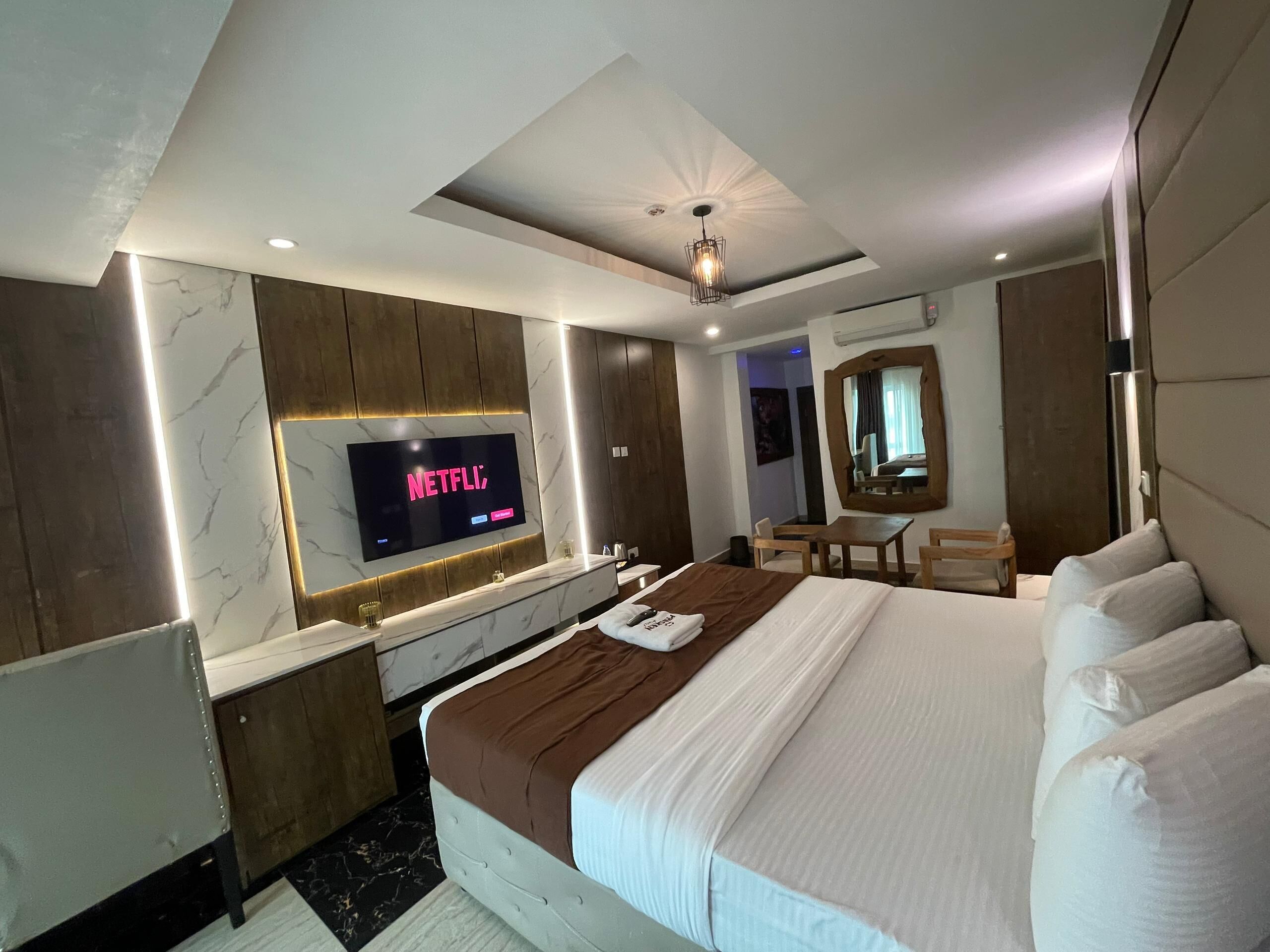 Une chambre d’hôtel moderne avec un grand lit, un téléviseur affichant « NETFLIX », un bureau et un miroir.