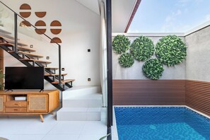 Un intérieur moderne avec un escalier, un téléviseur à écran plat et un espace piscine agrémenté de jardinières murales végétalisées.