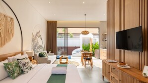 A modern hotel room with a large bed, a TV, a seating area with a table, and a balcony with plants. - Cove Anantaha Loft & Villa (Keroboken Kelod)