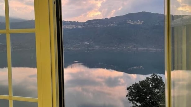 A view through a window with yellow frames, reflecting a landscape with a body of water, trees, and distant hills. - House with a view of Lake Nemi  (Genzano di Roma)