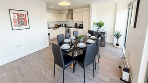Een moderne keuken met witte kasten, een eethoek met een ronde tafel en stoelen, en een kleine plant in een pot op het aanrecht.