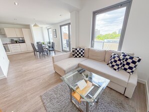 A modern living room with a sofa, a glass coffee table, and a view of the city through large windows. - Hoxton 3Bedroom Penthouse w/ Balcony & Lift near Shoreditch, Hackney, Old Street (London)