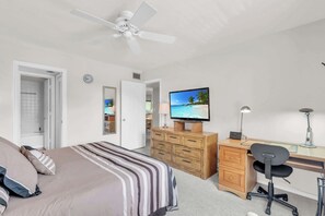 Ein Schlafzimmer mit Bett, Schreibtisch, Sessel, Fernseher und Deckenventilator.