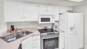 A modern kitchen with white cabinets, a stainless steel sink, a microwave, a stove, and a refrigerator. - G-244 - Resort and Pool Views & Sleeps 4 (Naples)