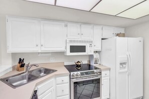 A modern kitchen with white cabinets, a stainless steel sink, a microwave, a stove, and a refrigerator. - G-244 - Resort and Pool Views & Sleeps 4 (Naples)