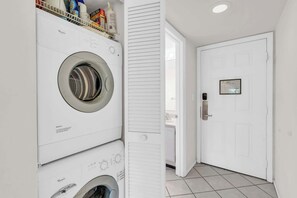 A laundry area with a front-loading washer and dryer, a white door with a peephole, and a tiled floor.
