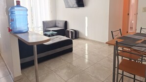 Ein modernes Wohnzimmer mit einer Couch, einem Couchtisch, einem an der Wand befestigten Fernseher und einem Essbereich mit Stühlen und einem Tisch.