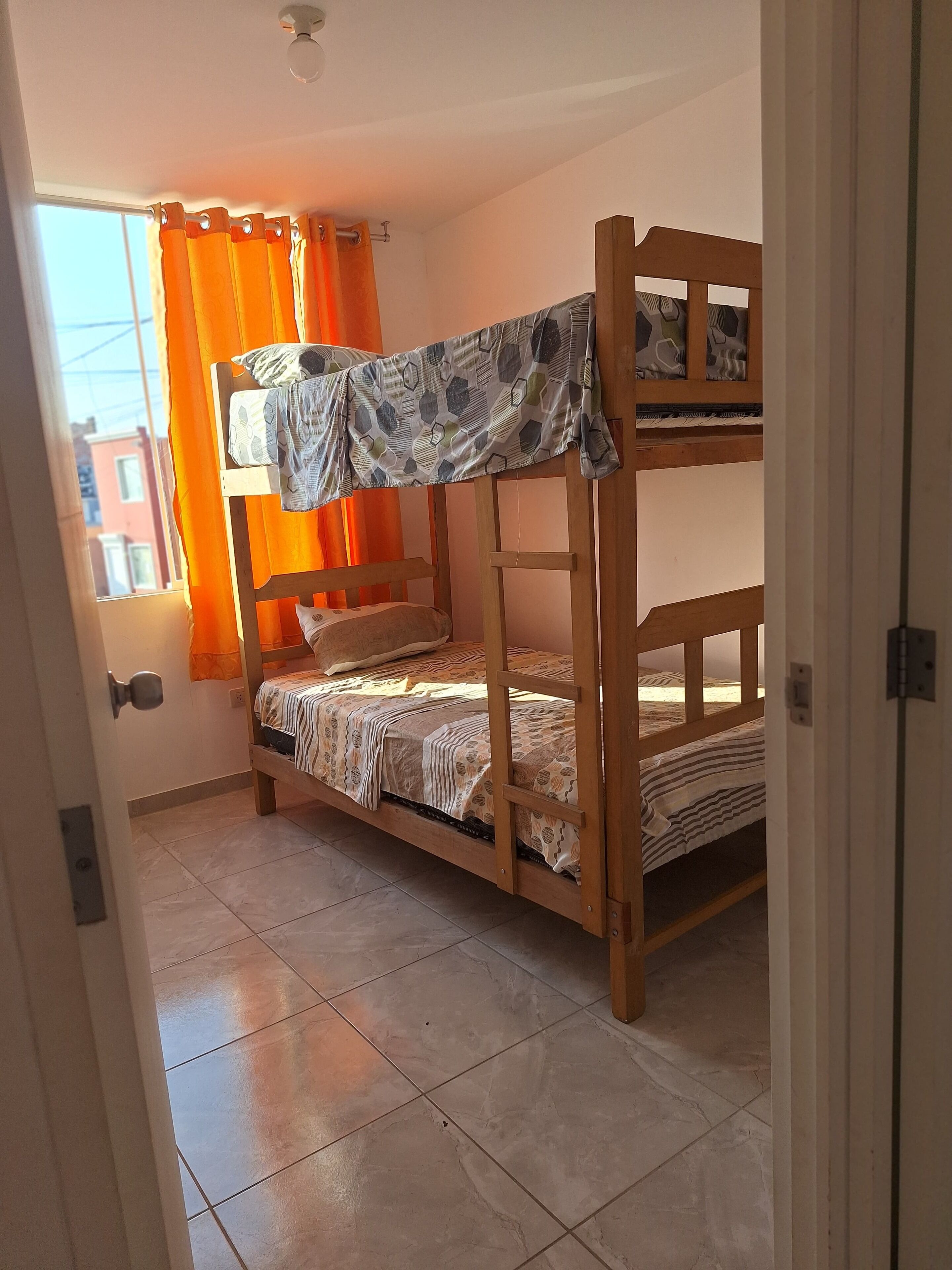 A bunk bed room with orange curtains, a tiled floor, and a view of buildings outside.