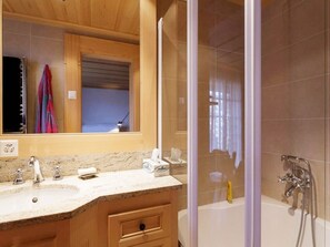 Une salle de bain avec un meuble-lavabo en bois, un grand miroir, une douche avec une porte en verre et une baignoire.