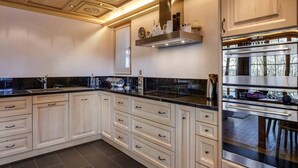 A modern kitchen with white cabinetry, black countertops, and stainless steel appliances. - Lush Apartment With Sauna and hot tub (Saanen)