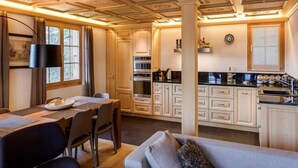 A compact kitchen with white cabinets, a dining area with a table and chairs, and a sofa with a throw pillow. - Lush Apartment With Sauna and hot tub (Saanen)