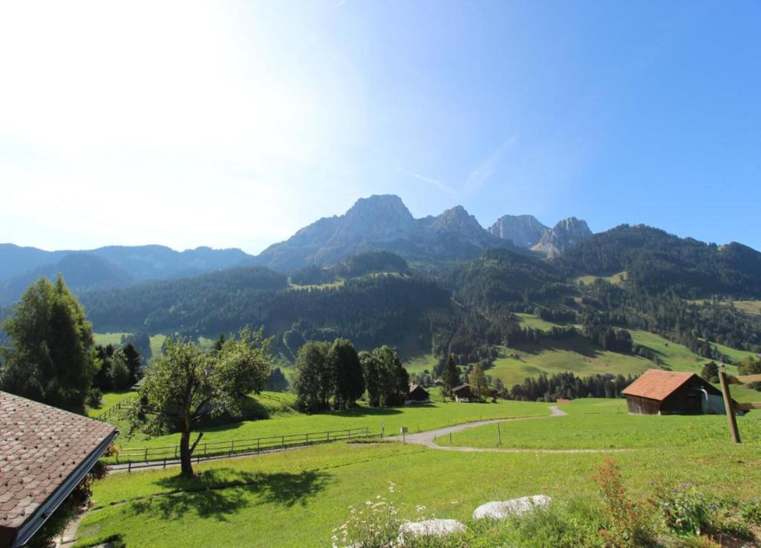 A rural landscape with a house, a fenced field, and mountains in the background.
