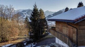 A wooden cabin with a snow-covered roof, surrounded by trees and mountains in the background. - Lush Apartment With Sauna and hot tub (Saanen)