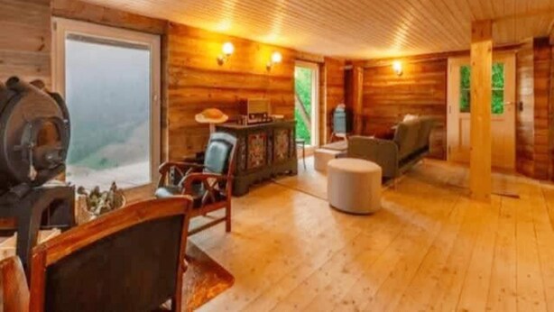 A wooden cabin interior with a large window, a fireplace, and a cozy seating area. - Chalet in Gstaad Near Ski Slopes (Rossiniere)
