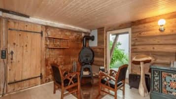 A rustic wooden interior with a fireplace, two wooden chairs, a small table, and a decorative cabinet.