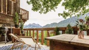 An outdoor patio with a wooden table and chairs, a barbecue grill, and a view of mountains. - Chalet in Gstaad Near Ski Slopes (Rossiniere)