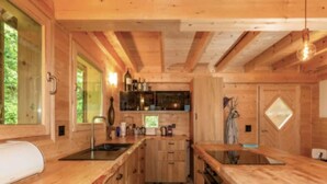 A wooden cabin kitchen with a central island, wooden cabinets, and a window overlooking greenery. - Chalet in Gstaad Near Ski Slopes (Rossiniere)