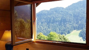 A room with a large window offering a view of a forested mountain. - Chalet in Gstaad Near Ski Slopes (Rossiniere)