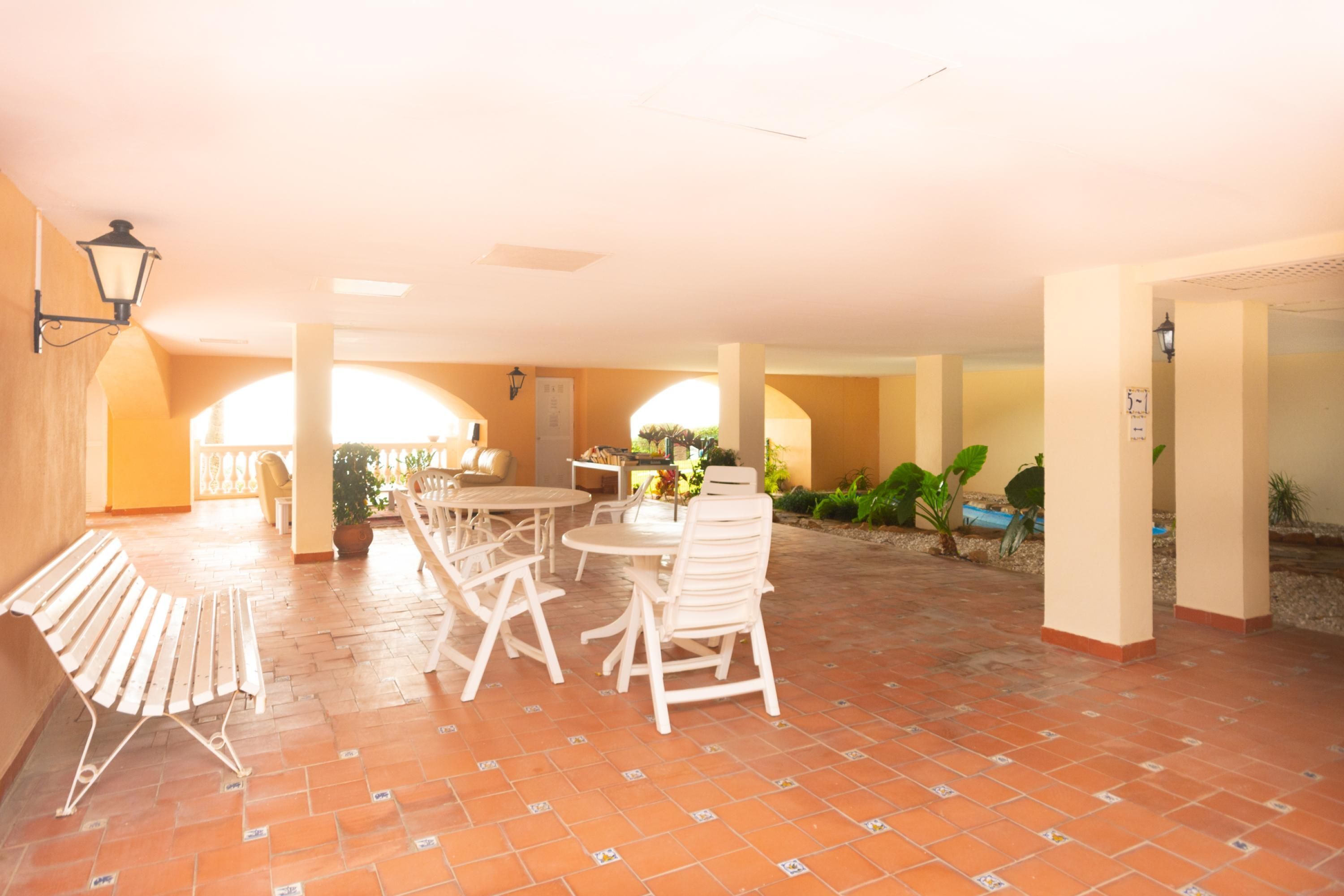 A spacious patio with a round table and chairs, surrounded by potted plants and a bench.