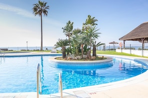 Une piscine agrémentée d’un palmier et d’une structure à toit de chaume.