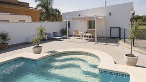 A swimming pool with a geometric tile border, surrounded by a patio with lounge chairs and a table.