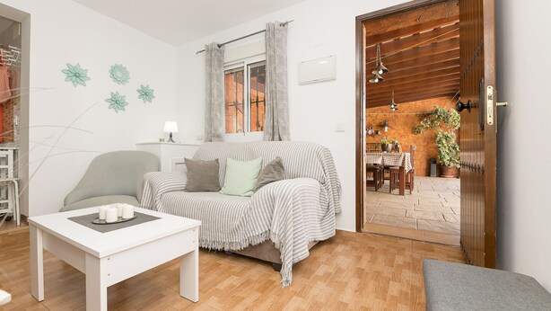 A cozy living room with a sofa, a coffee table, and a dining area visible through an open door.