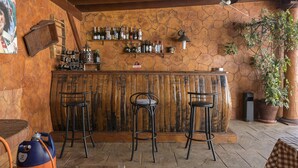 A rustic bar area with wooden stools, a stone wall, and a variety of bottles on shelves.