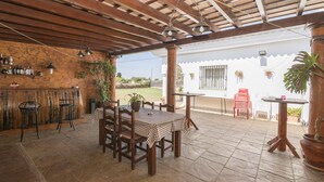 A covered patio area with a stone wall, wooden furniture, and hanging plants.