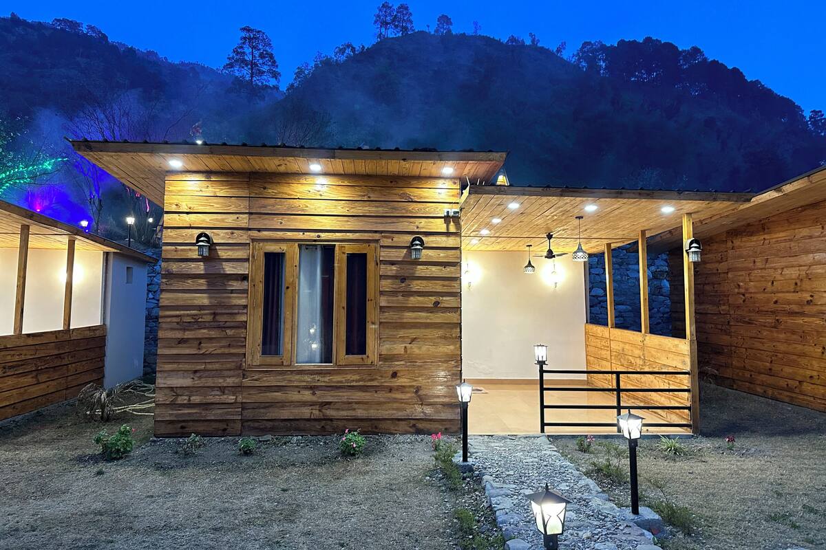 Uma cabana de madeira com varanda coberta, paredes de pedra e um caminho de cascalho.